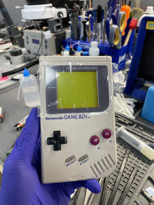 Original Game Boy opened on the repair bench, held in a gloved hand