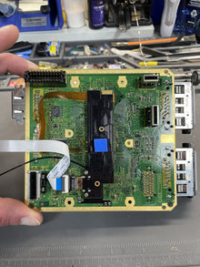 Console mainboard lifted out of its shell and held over the bench