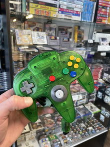 Clear green Nintendo 64 controller held up in front of the shop's game shelves