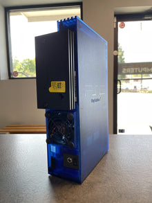 Translucent blue PlayStation 2 seen from an angle with the drive door open